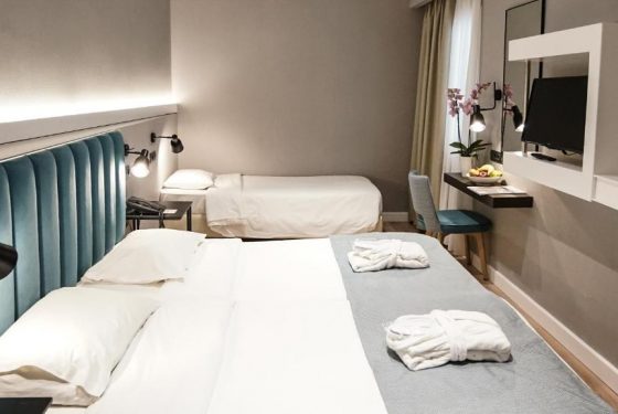 Side view of double bed, single bed, desk, chair, TV and bathrobes neatly folded on the beds of the Standard Room Triple
